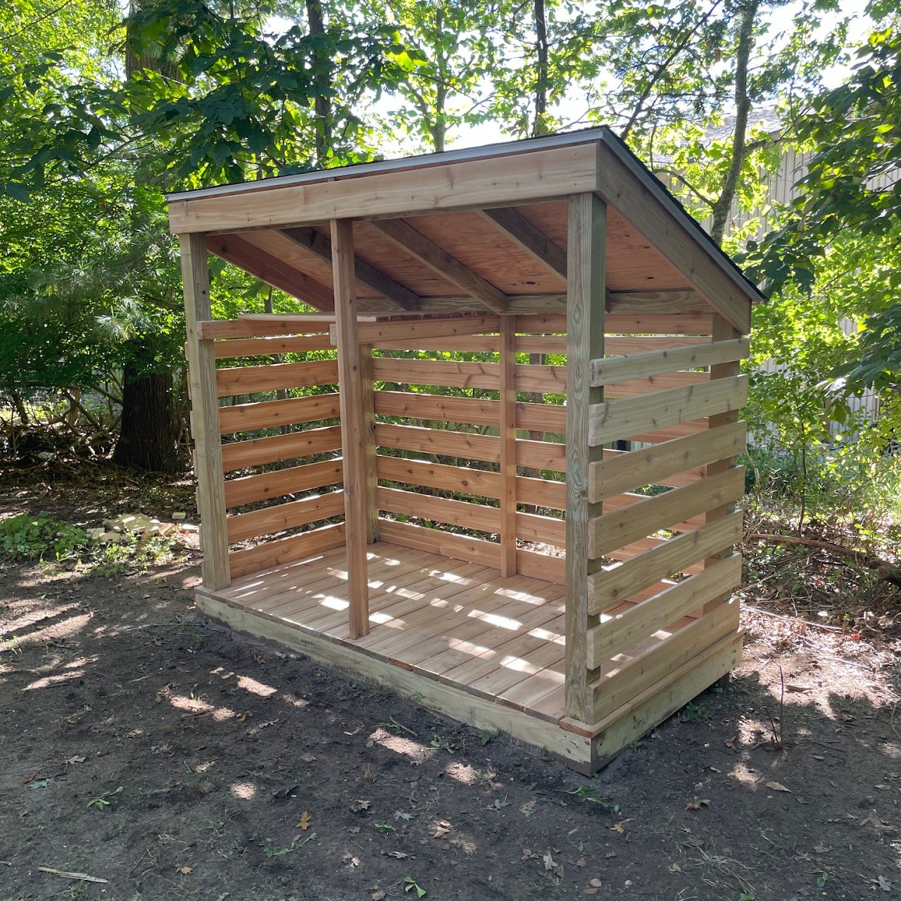 Finished open-front wood firewood shed with shingled roof in backyard