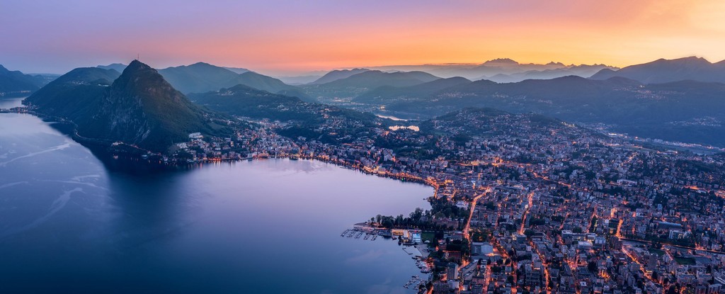 A view of a city on the edge of a body of water at sunset in a mountainous region