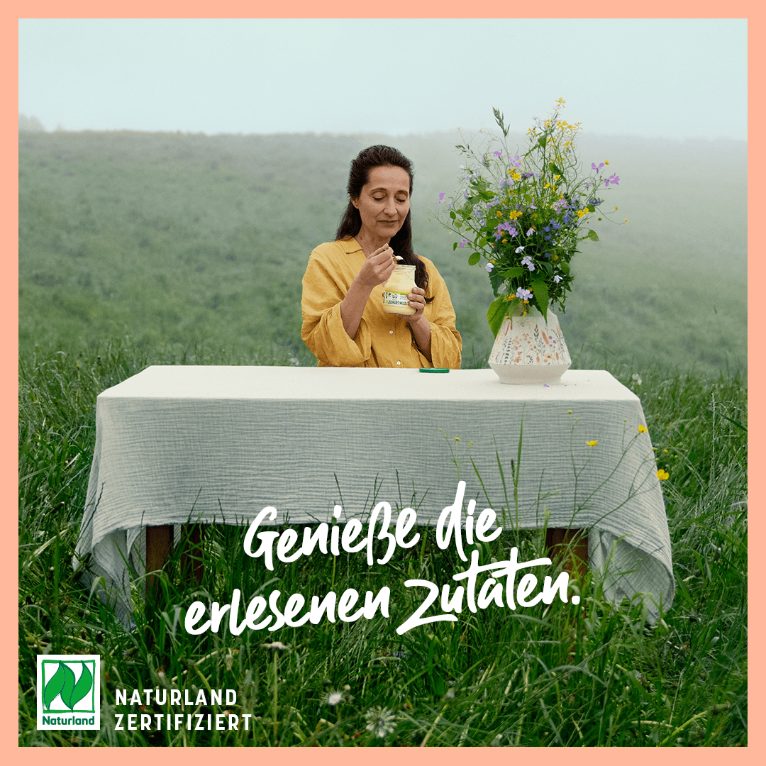 Woman enjoying organic yoghurt outdoors in a wildflower meadow, connecting the product to its natural origins.