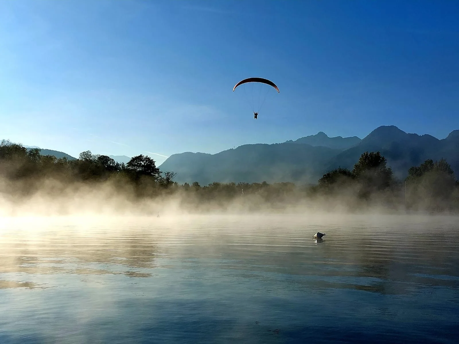 Paraglider flying over a misty mountain lake