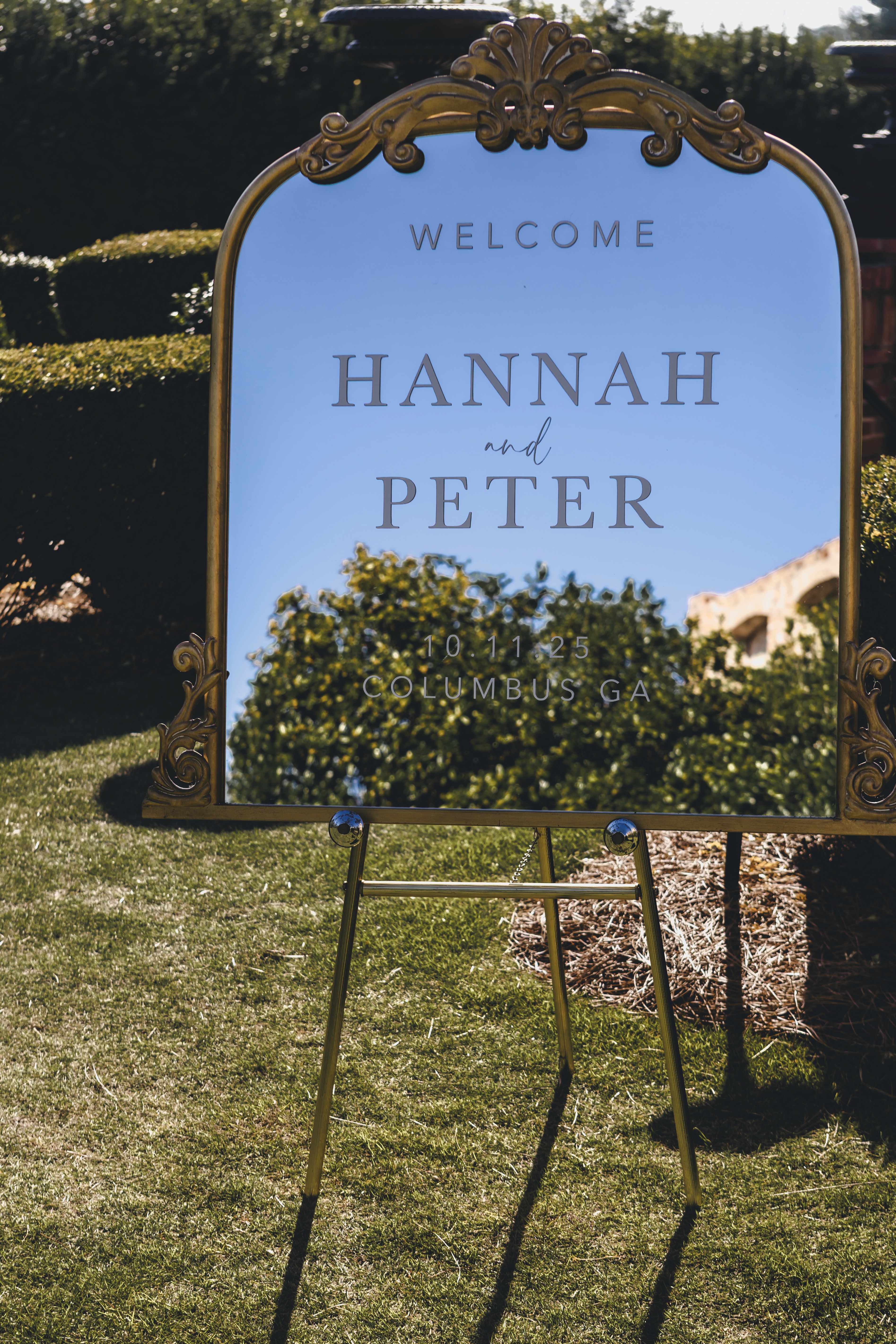 Framed welcome sign for Hannah and Peter displayed outdoors on the wedding lawn.