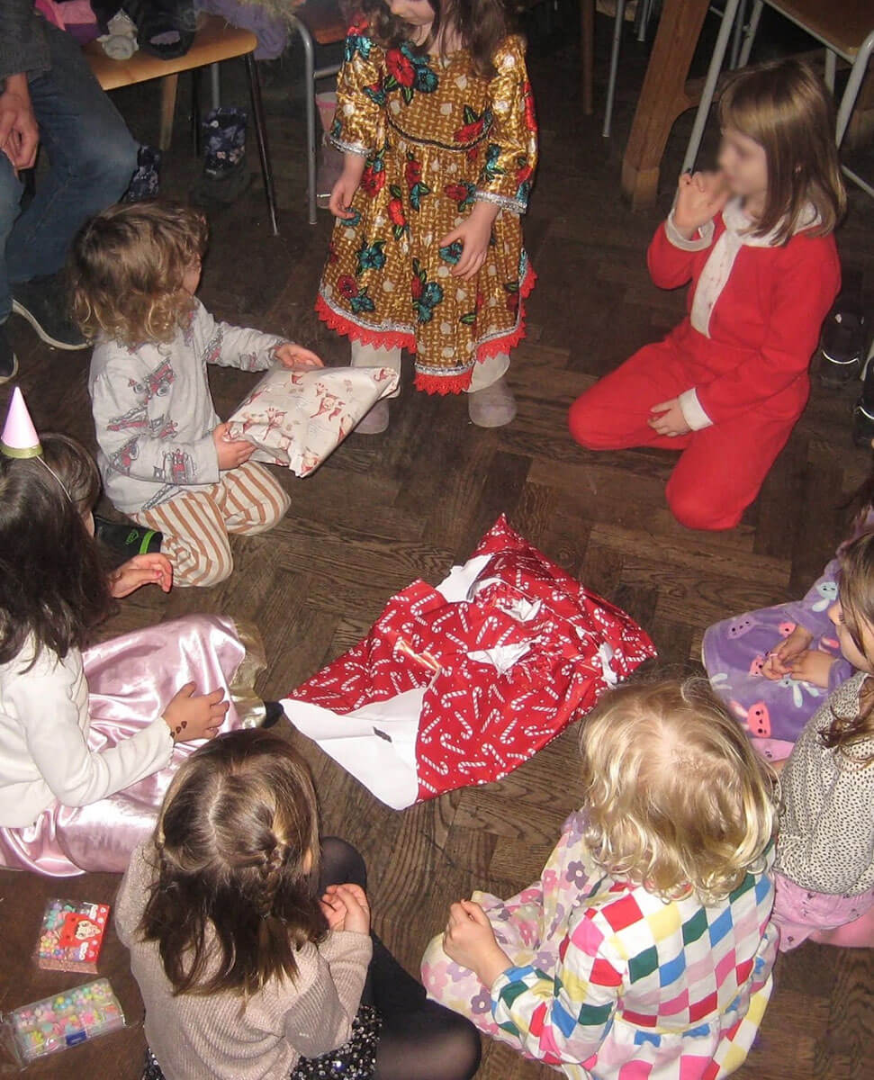 Children gathering on the ground watching one child unwrap gifts.