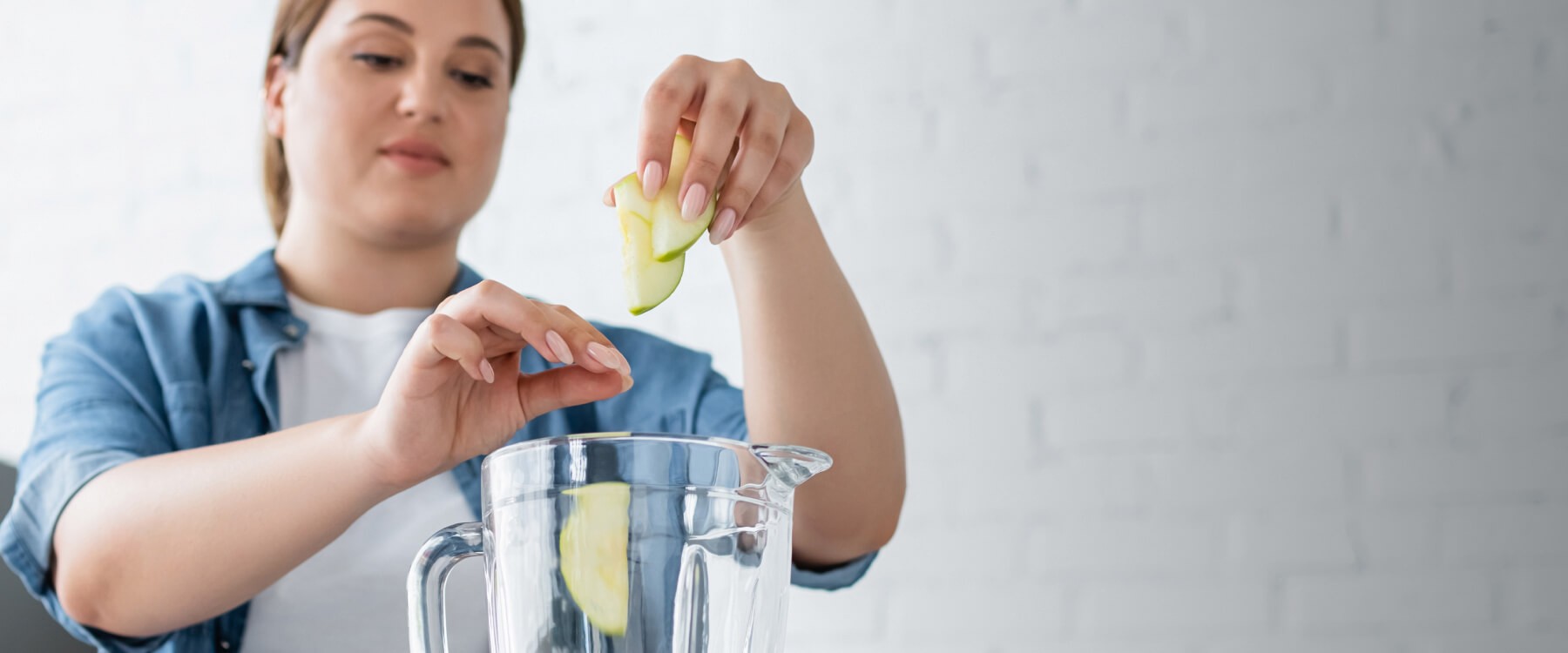 A woman placing apples in a blender.