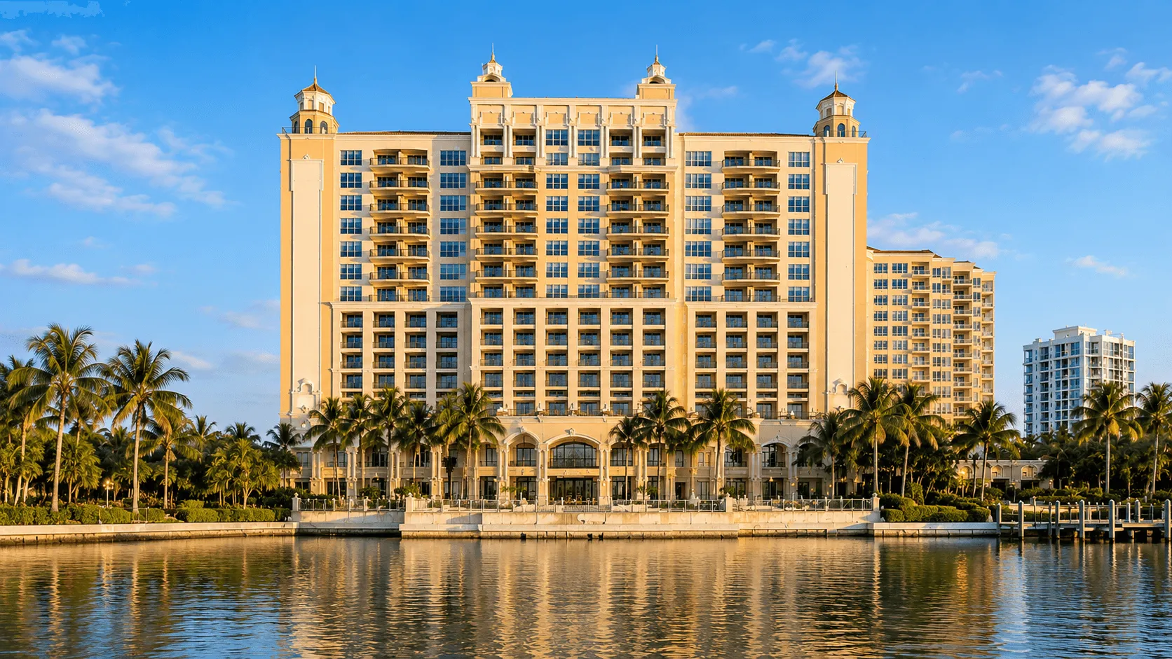 Tall tan building with balconies and palm trees on water