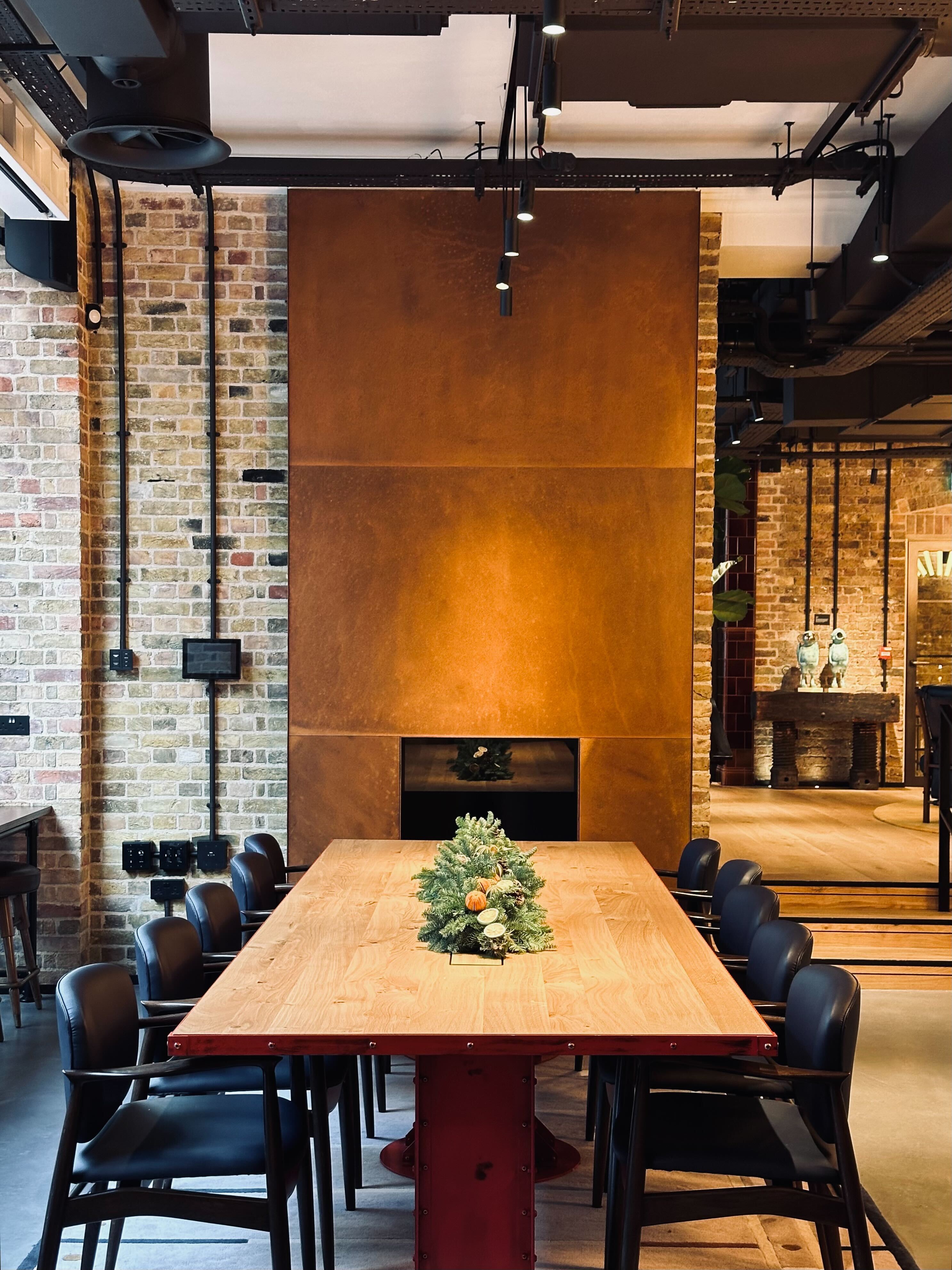 Warmly lit conference room with a long wooden table, black chairs, and a fireplace in the background
