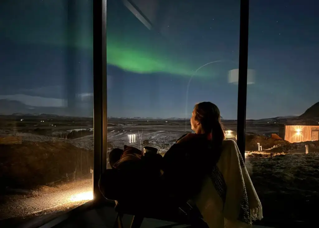 Reykjavik's city lights glowing orange on the horizon beneath a green aurora borealis on a clear winter night