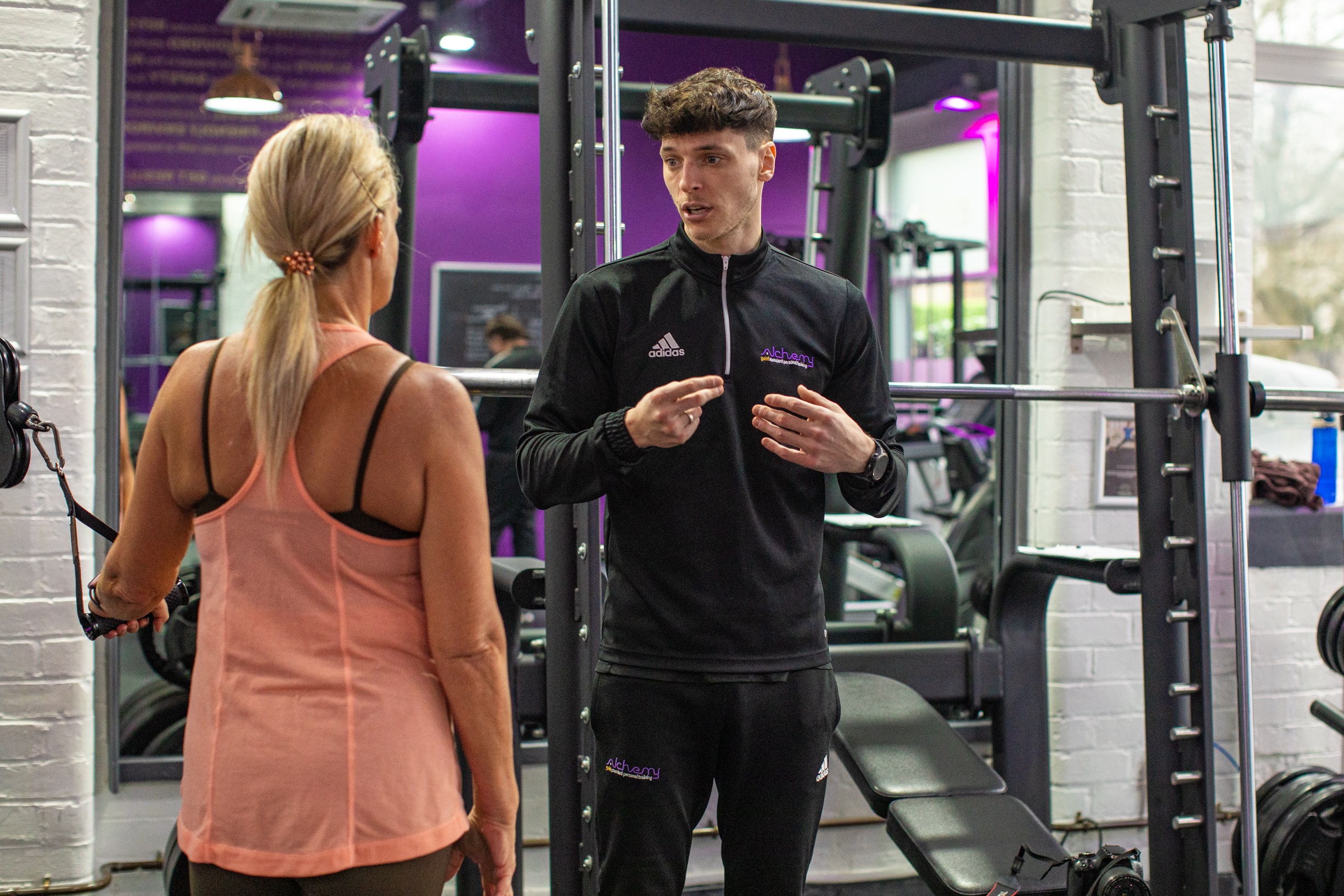 An Alchemy personal trainer in Wilmslow and a woman share a discussion in a gym environment, emphasizing teamwork and motivation