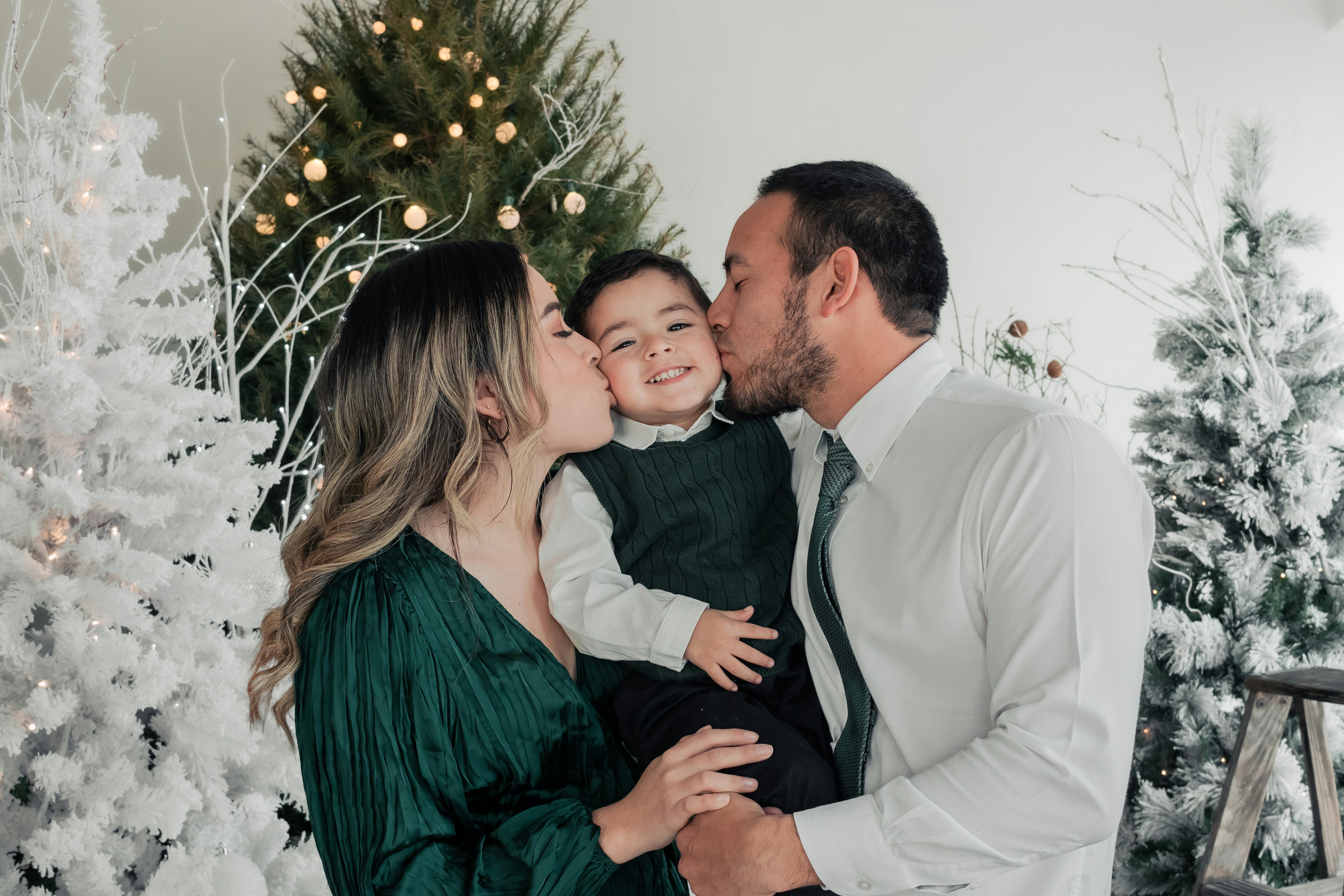 a man and woman kissing a child in front of a christmas tree
