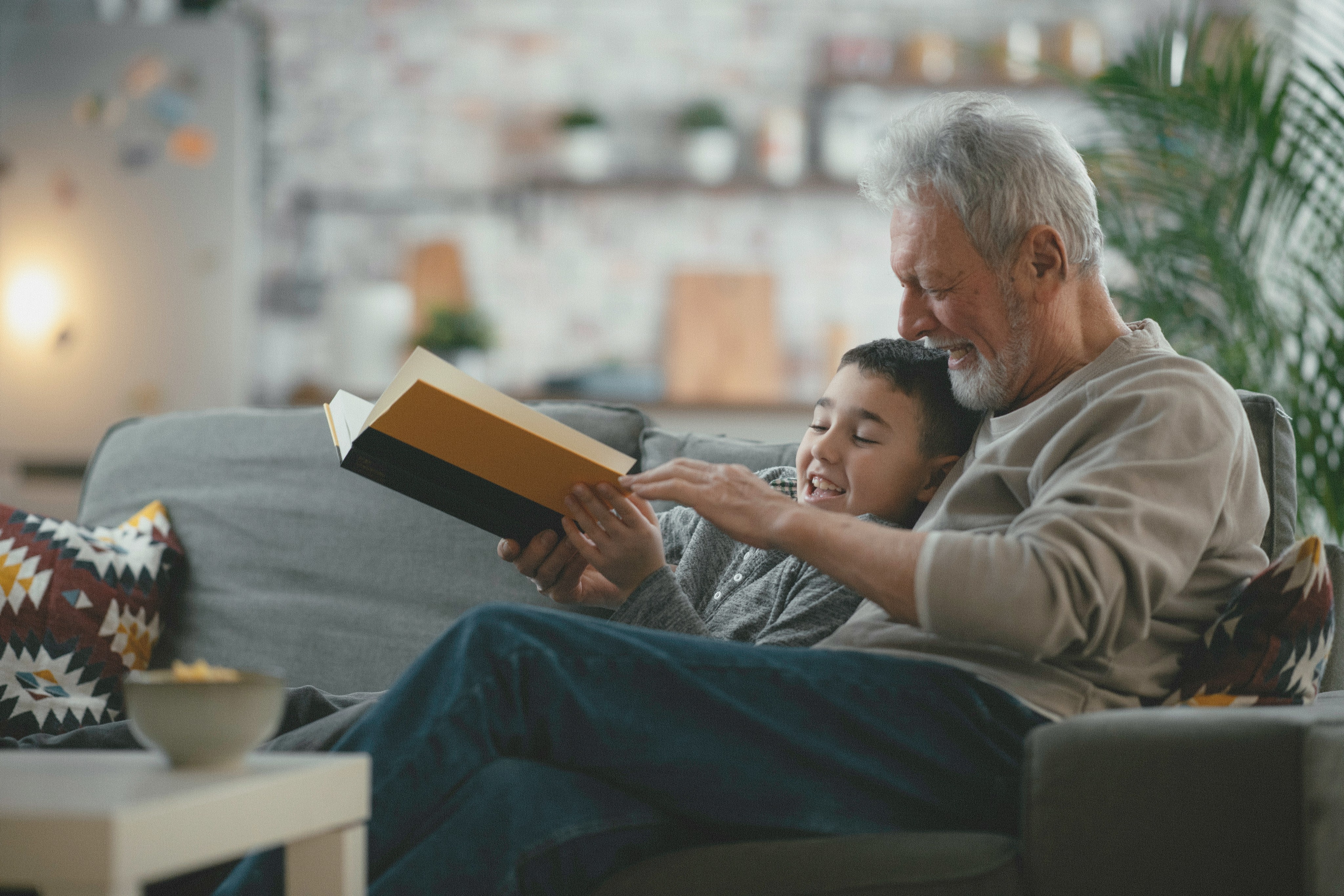 An older man and a young boy reading a book together on a sofa at home