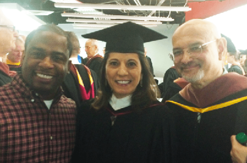 A photo of three people in a hall, one of them just graduated.