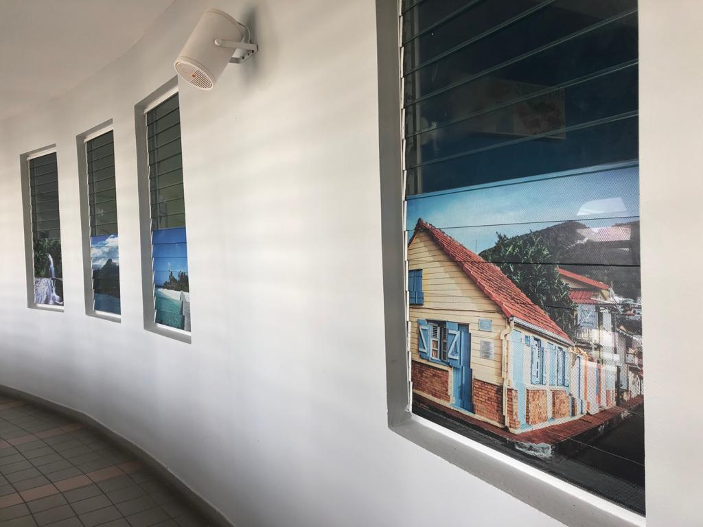 Couloir incurvé avec quatre petites fenêtres. Chaque fenêtre offre une vue différente, notamment sur une maison et des paysages. Ambiance lumineuse et aérée.