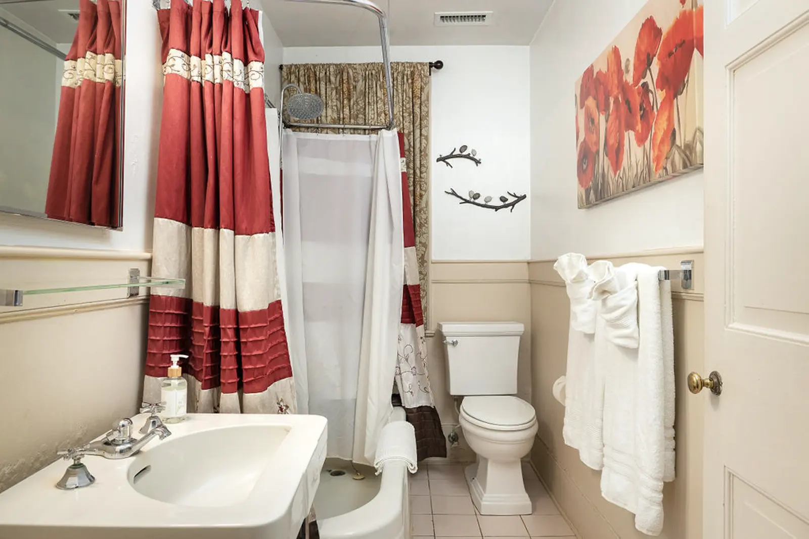 A warm bathroom with a white sink, toilet, shower, and red poppy artwork.