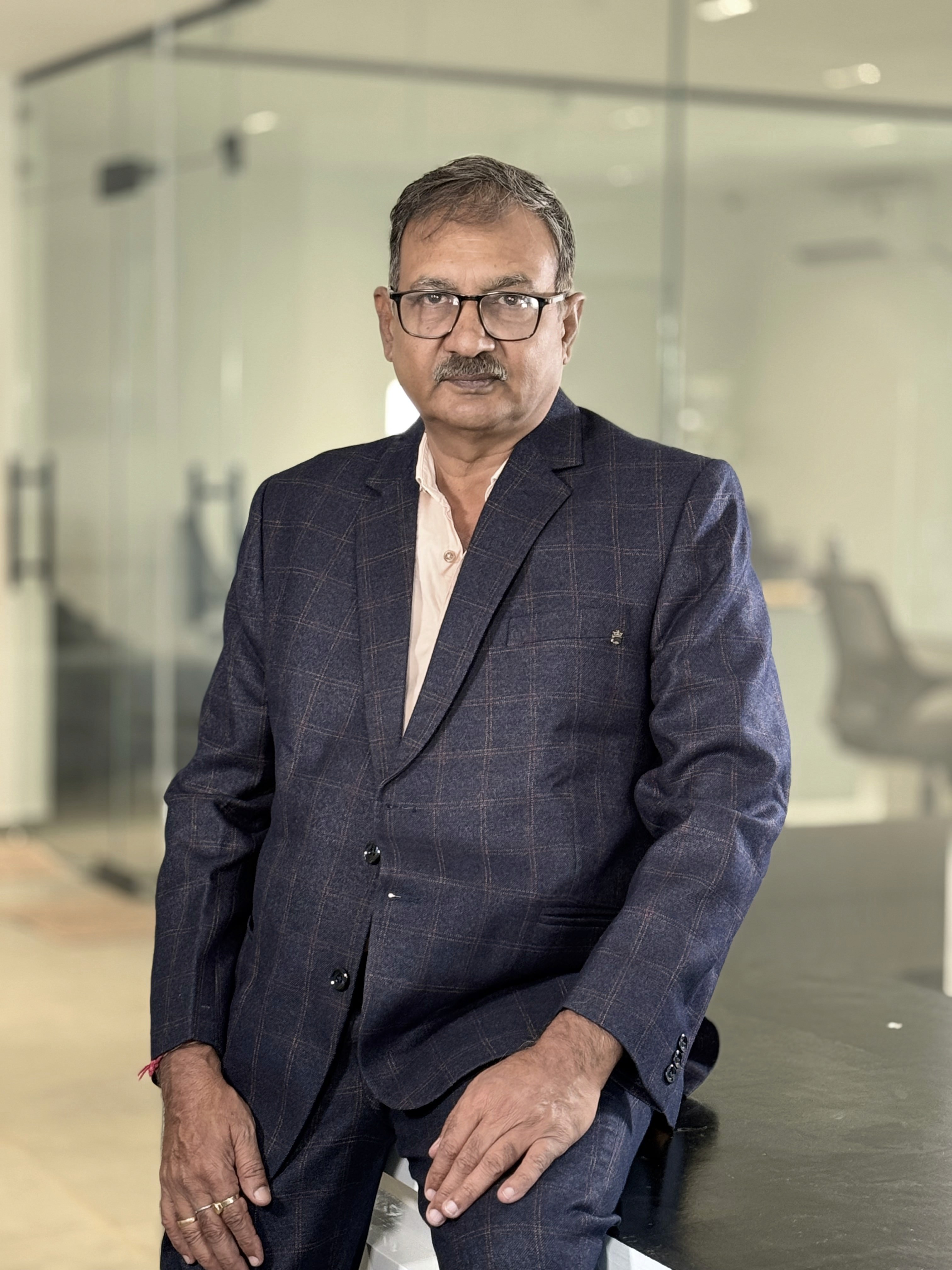 A person with blond hair wears a dark coat and a beige turtleneck sweater. They have a calm expression, against a neutral background.