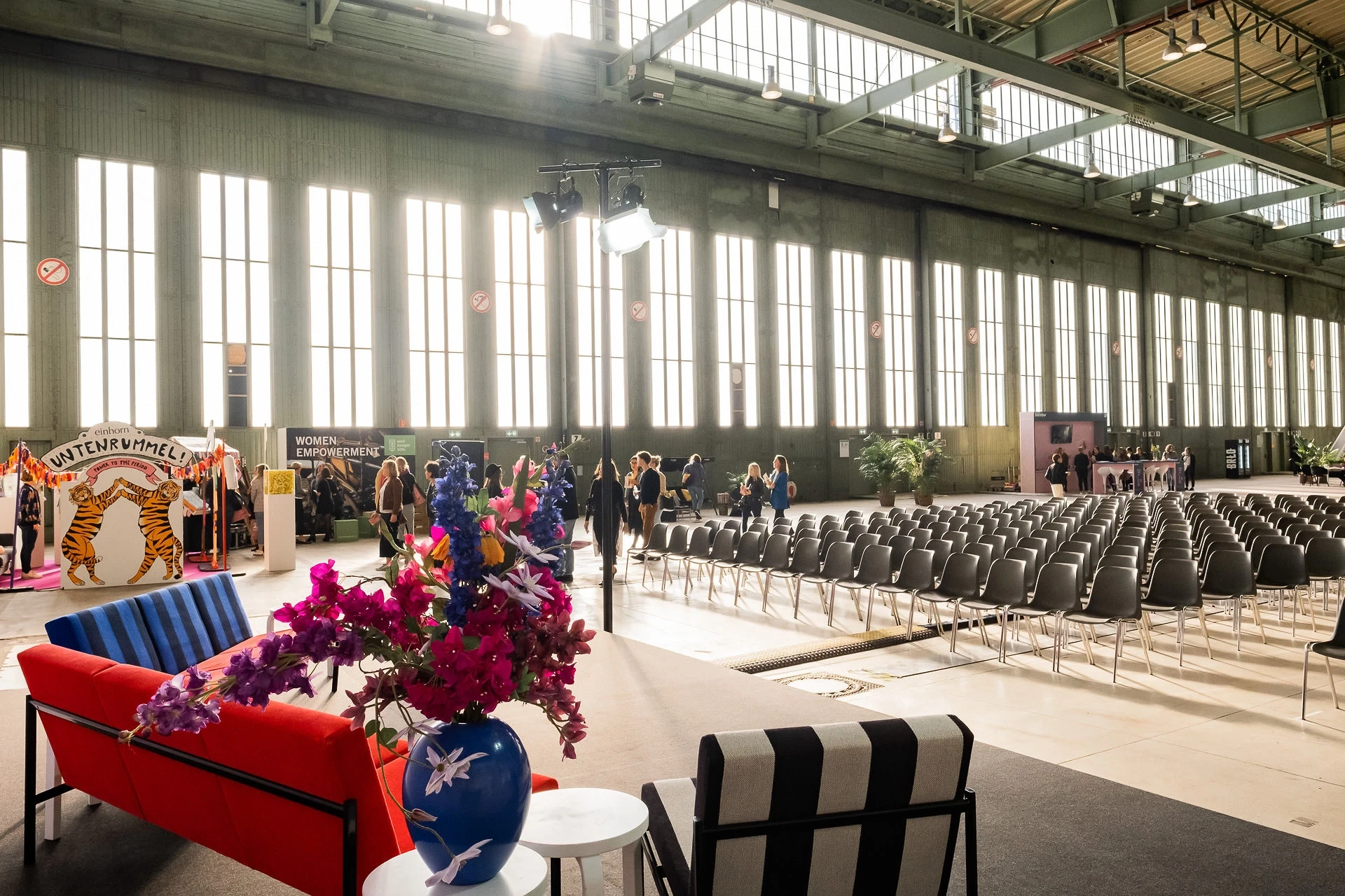 Colorful lounge seating with flower vases in front of the seating area along the window front of the Tempelhof hangar at Female Future Force Day.