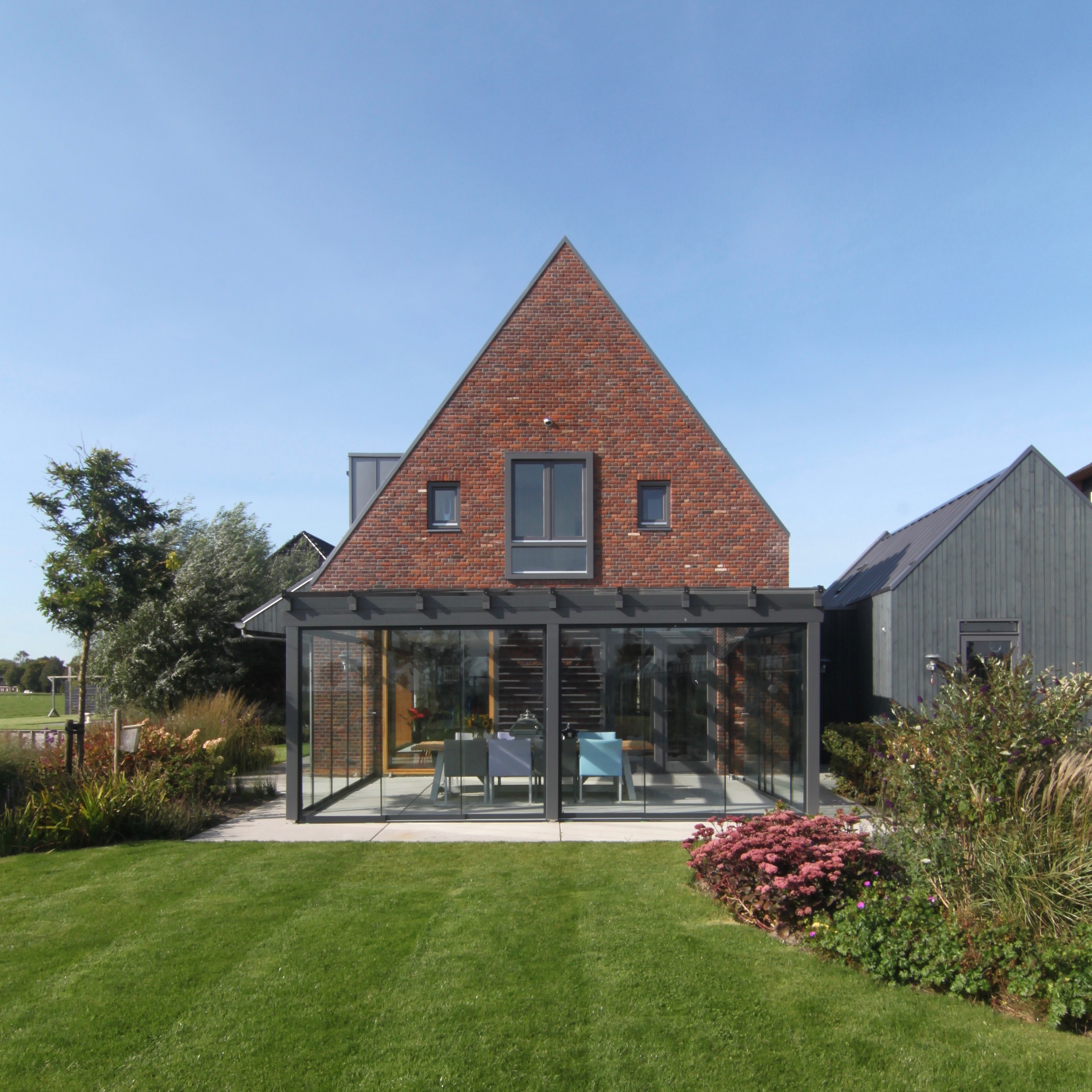 Een huis met een glazen uitbouw en een groene tuin op een heldere dag.
