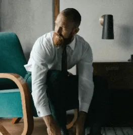 man in white dress shirt and black dress pants standing beside brown wooden chair