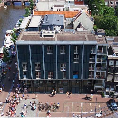 Aerial view of a busy street beside a canal, featuring a modern black building with large windows and people walking below.