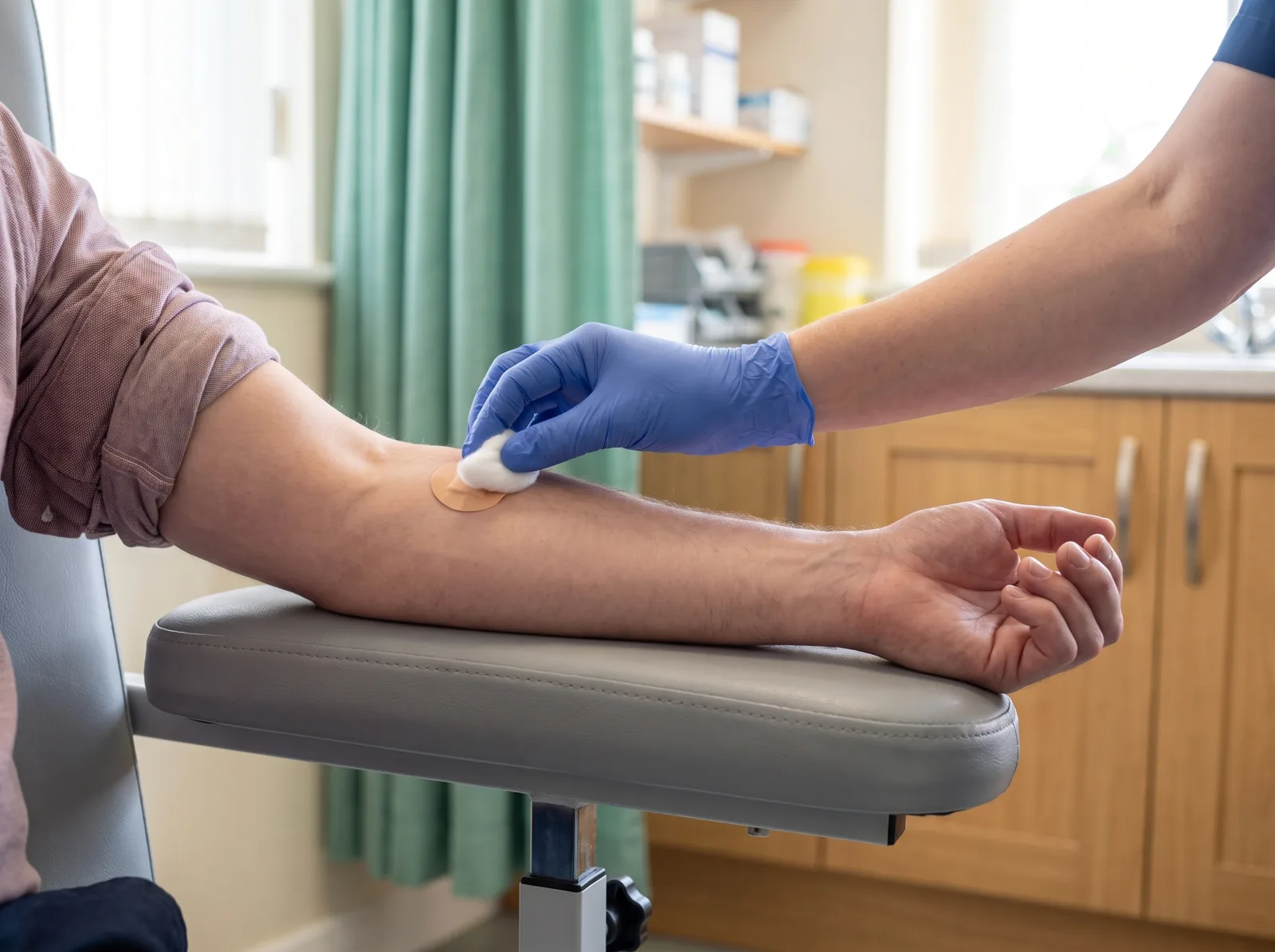 Cotton wool being pressed on a plaster on a patient's inner elbow after a blood test