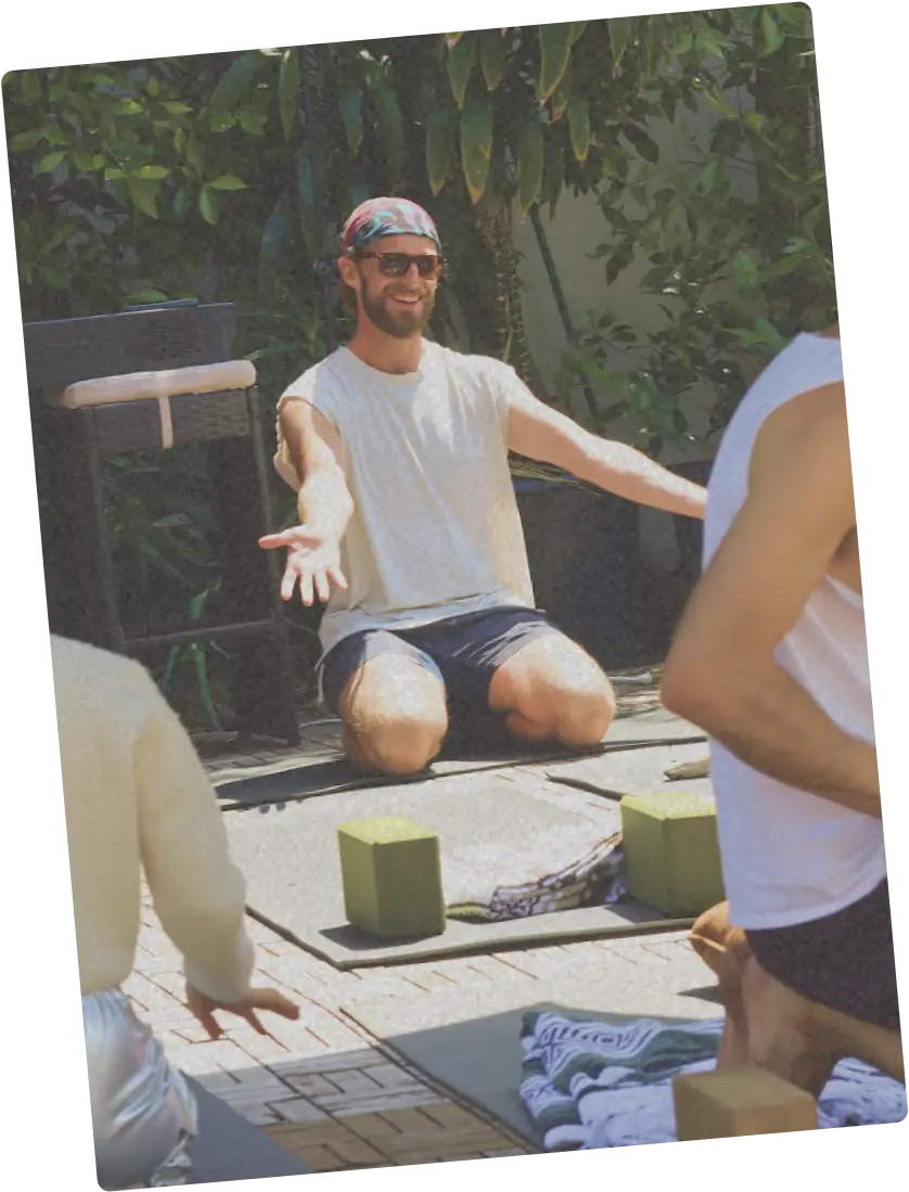 Person seated outdoors with arms extended, leading a yoga or movement practice with props.