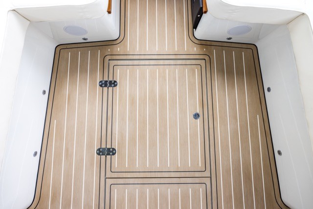 Overhead view of a motor yacht cockpit with a full EcoDeck light oak composite floor installation, featuring a precision-cut flush access hatch with stainless steel hinges and black caulking seams, showing EcoDeck's ability to integrate cleanly around deck hardware and openings
