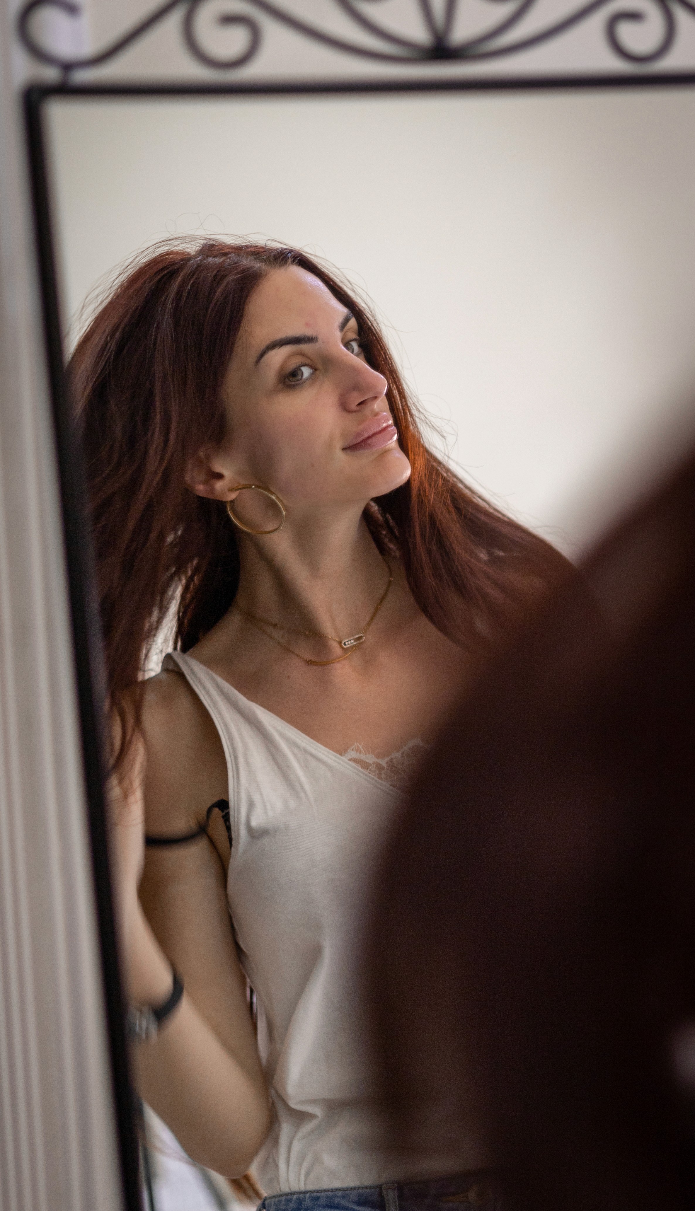 Woman looking into a mirror to admire her glowing skin after a Profhilo treatment.