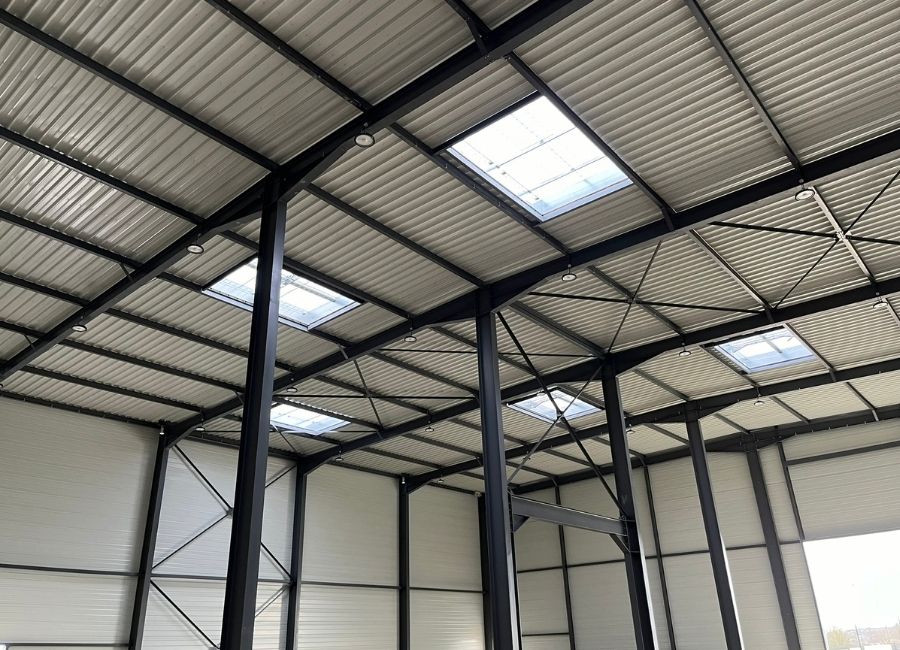Vue intérieure d’une charpente métallique avec éclairage naturel zénithal.