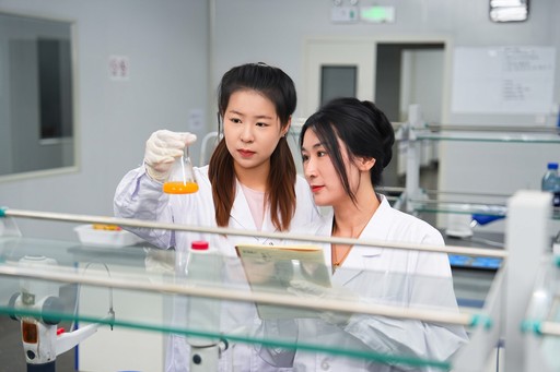 Two female scientists in white lab coats meticulously examine a flask of orange liquid, likely an egg product sample, in.