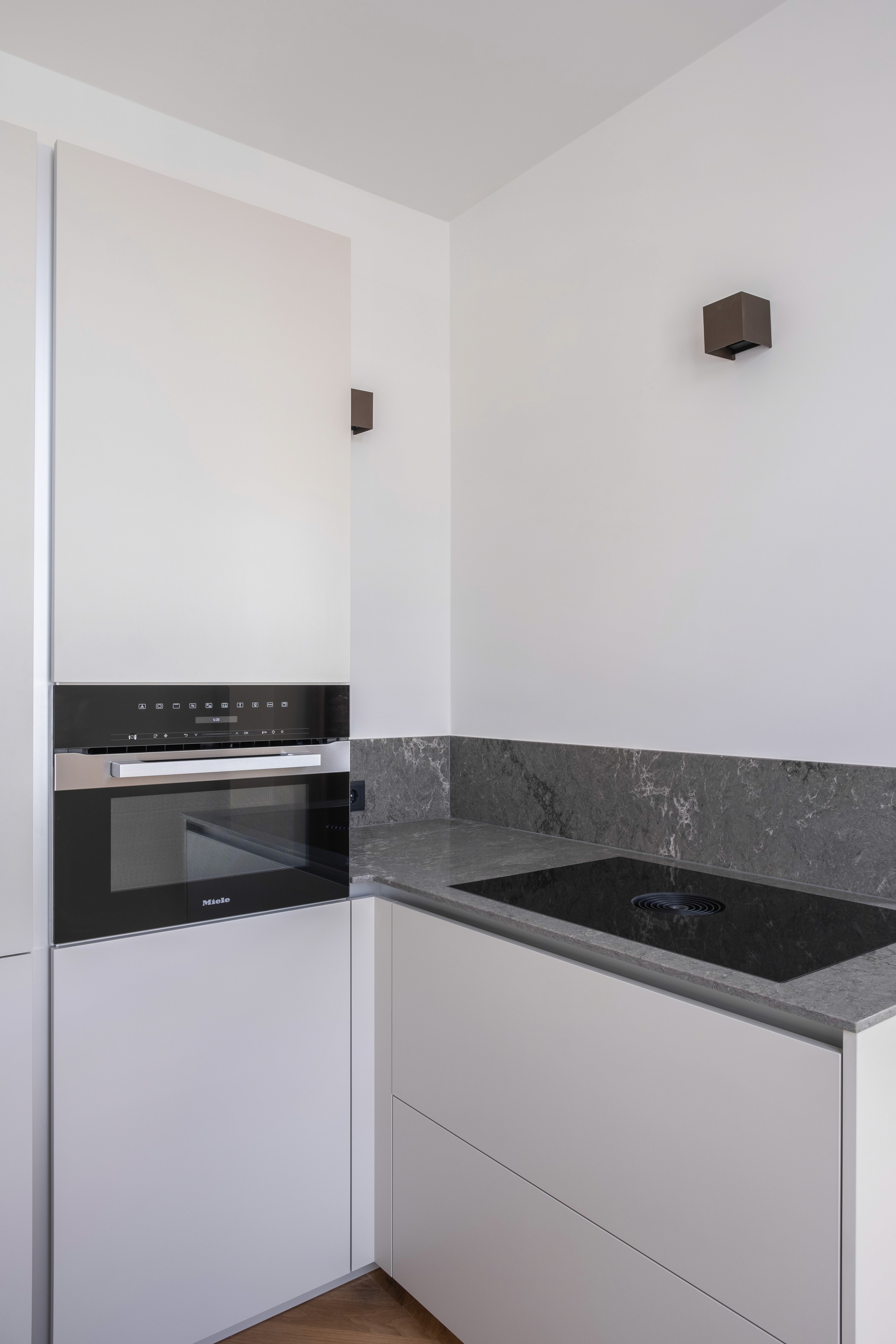 Kitchen detail with built-in Siemens oven, Bora induction hob, grey stone countertop, and bronze wall sconce