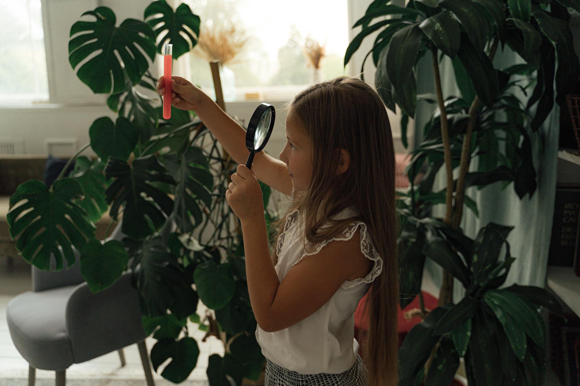 Young children wearing safety goggles using plastic magnifying glasses to examine green leaves and smooth stones.