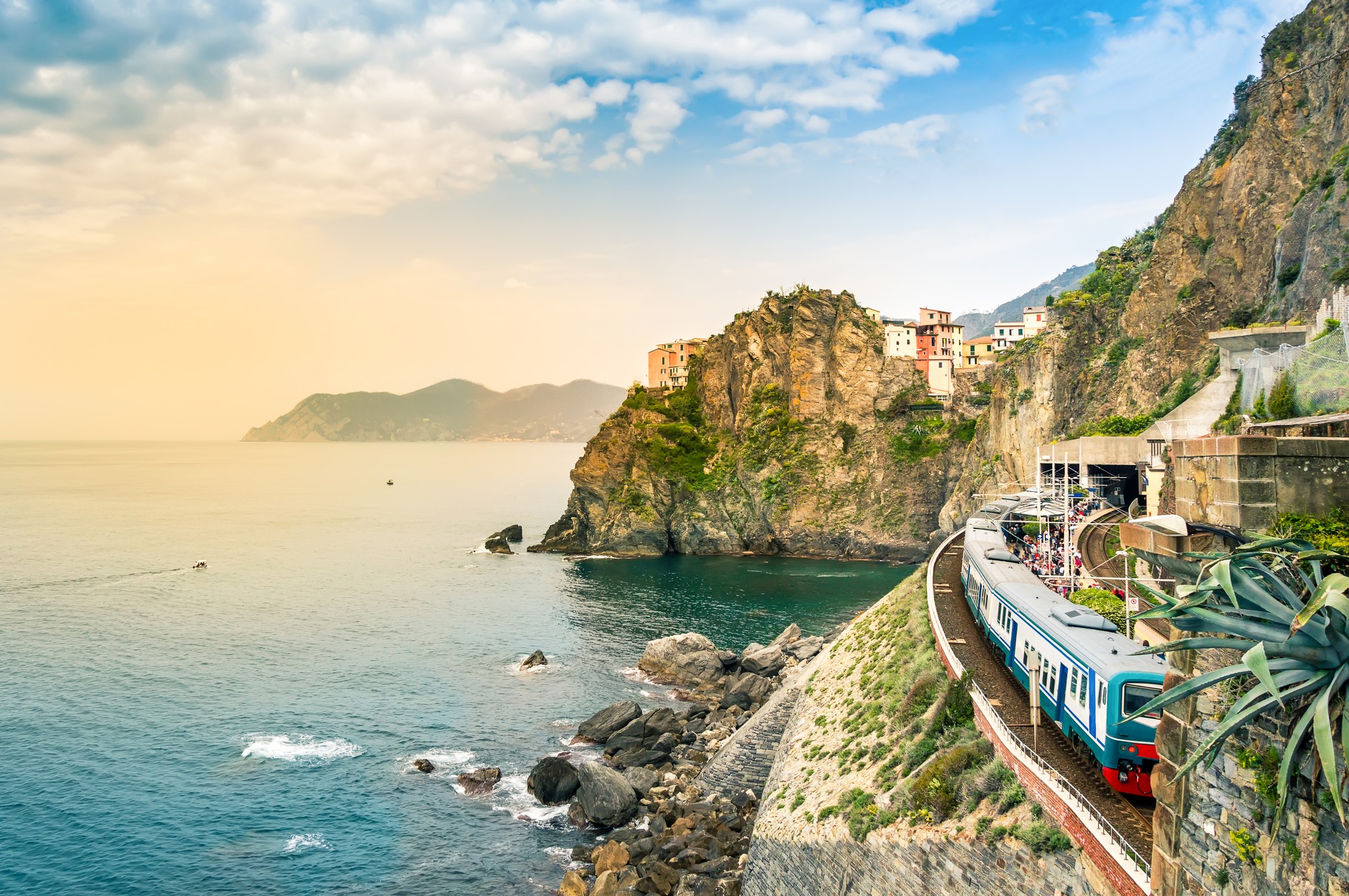 Train winding along the rugged Cinque Terre coastline with colorful cliffside houses and calm sea in the background.