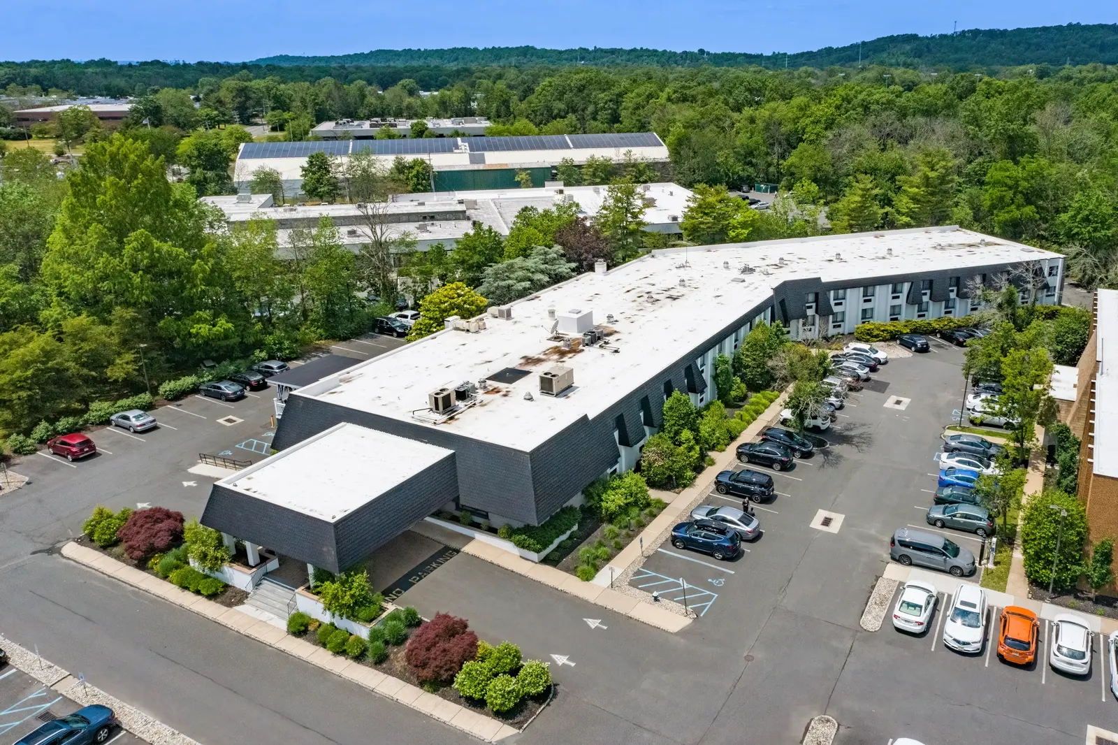 L-shaped commercial building with parking lots surrounded by trees.