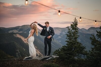 Tucker twirls Clemmie beneath string lights against pink evening clouds and mountains.