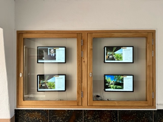 Four digital screens in a wooden display showing real estate listings.