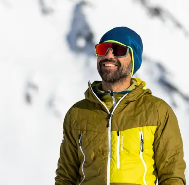 Mountain guide in the Mont Blanc area smiling in a snowy alpine environment, wearing technical winter clothing and sunglasses