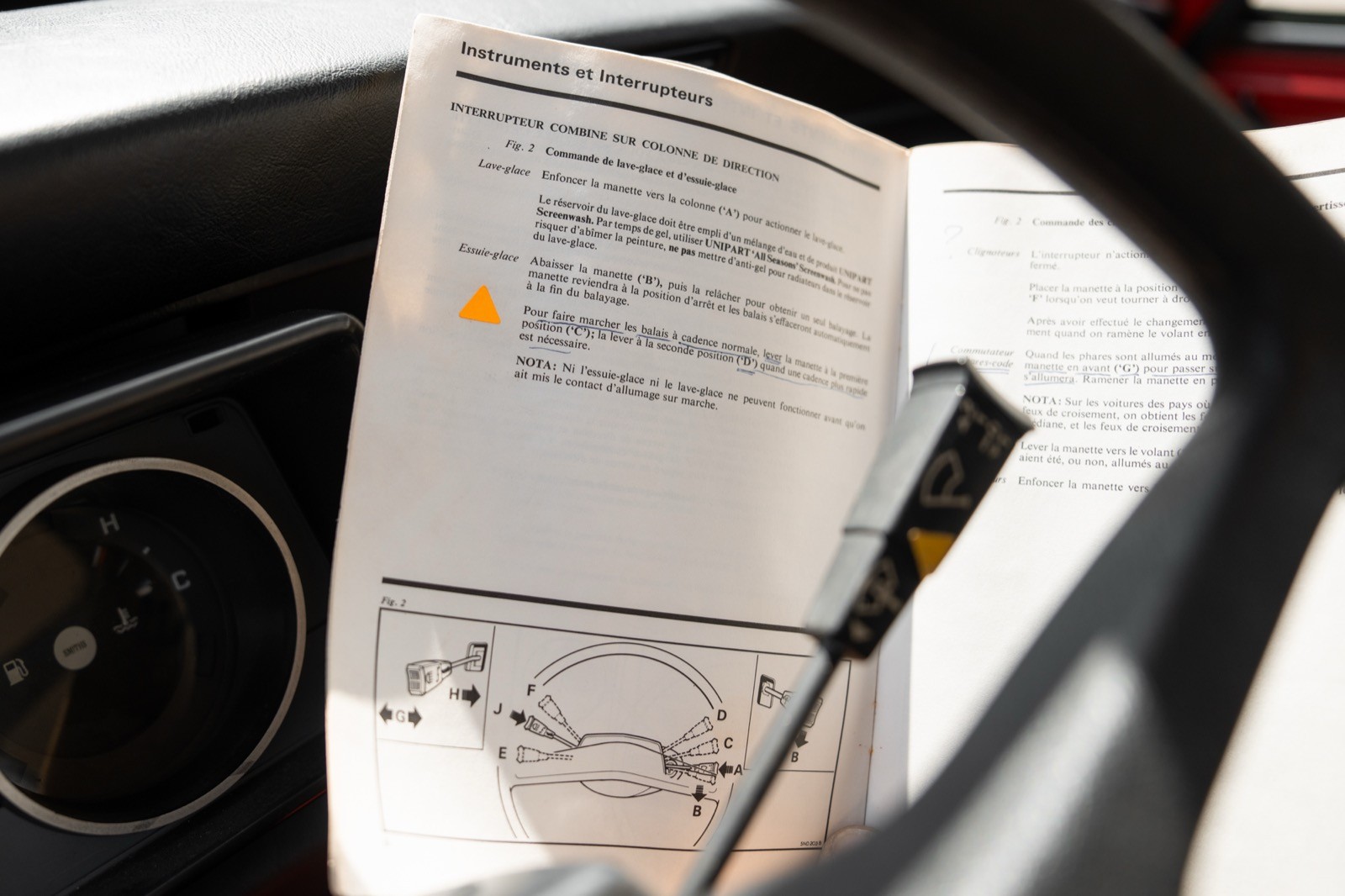 A document with text is clipped inside a car, next to a pen and part of the steering wheel visible.