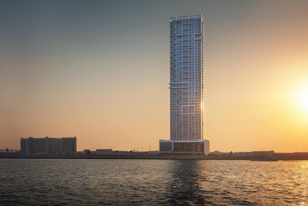 The Anwa Omniyat tower stands tall at sunset, seen from the water, surrounded by a stunning array of sunset hues.