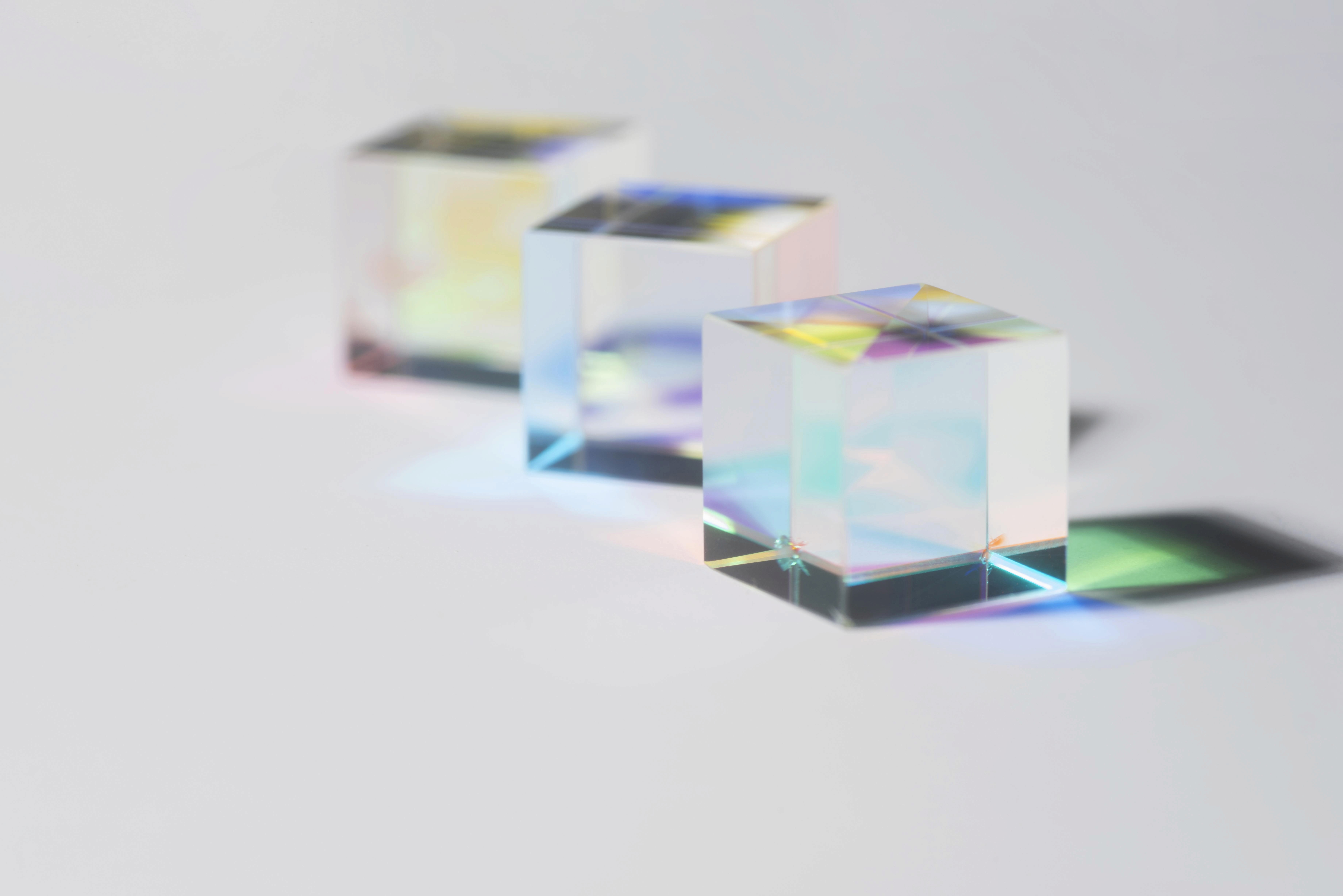 Three transparent glass cubes casting rainbow reflections on a white surface.