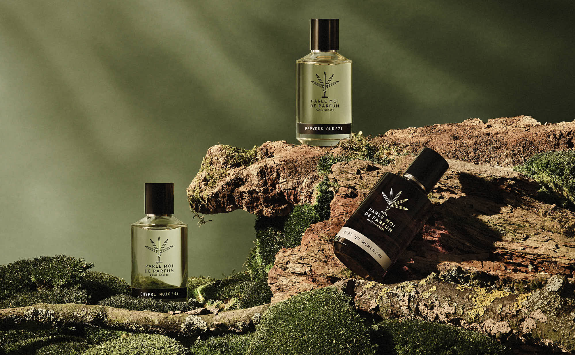 three perfume bottles are place on rocks and moss. Soft lighting enhances the scene.