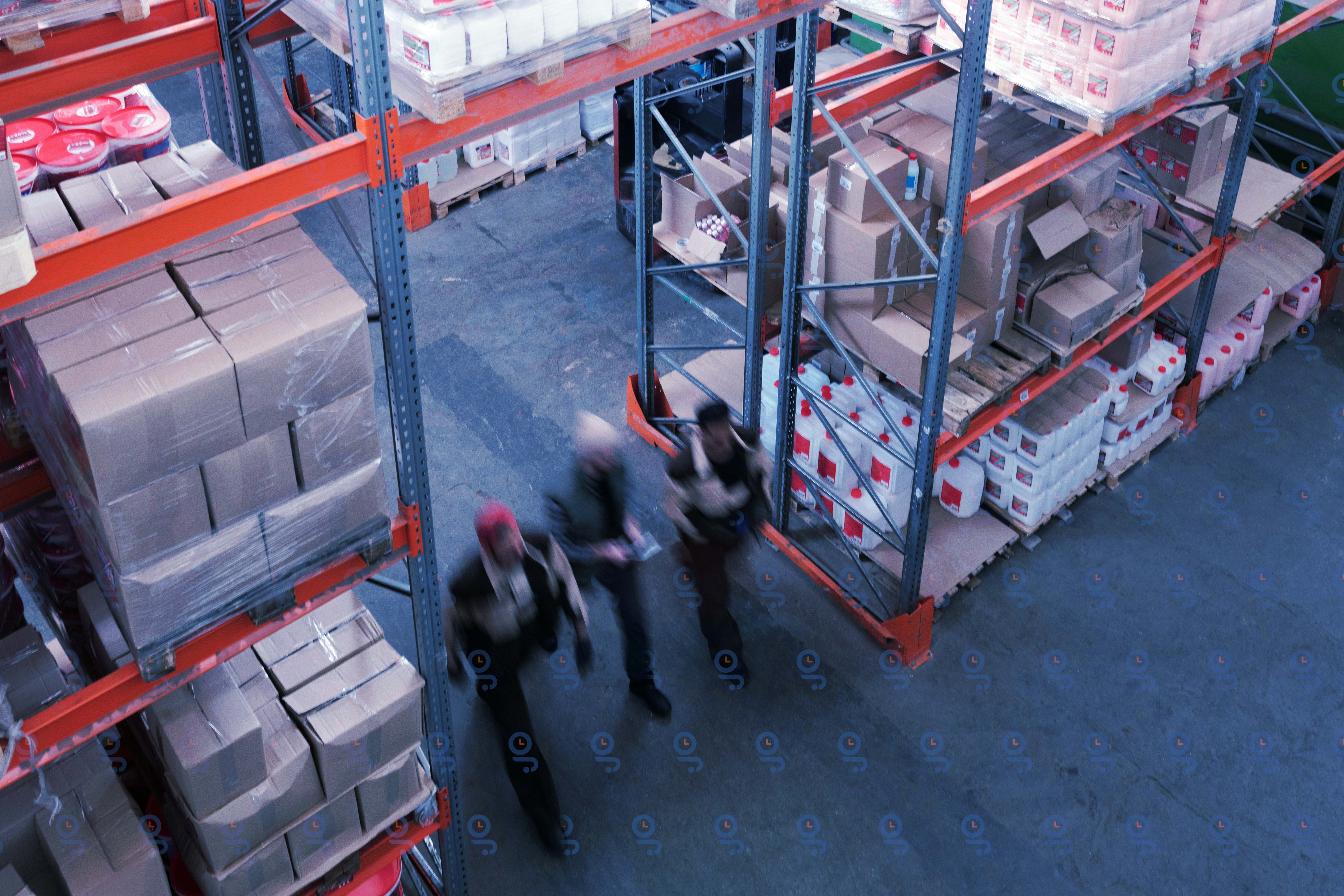 An aerial view of a group of people walking through a warehouse, with shelves and boxes arranged in the background.