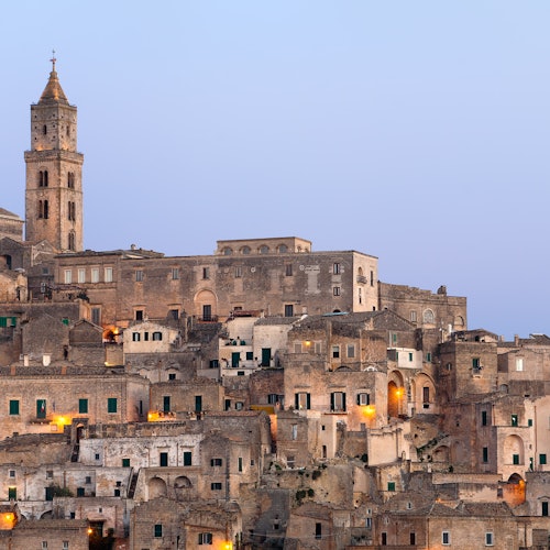 在一个晴朗的夜空下,这座古老的山坡小镇坐落着紧密排列的石头建筑和一座高耸的钟楼。