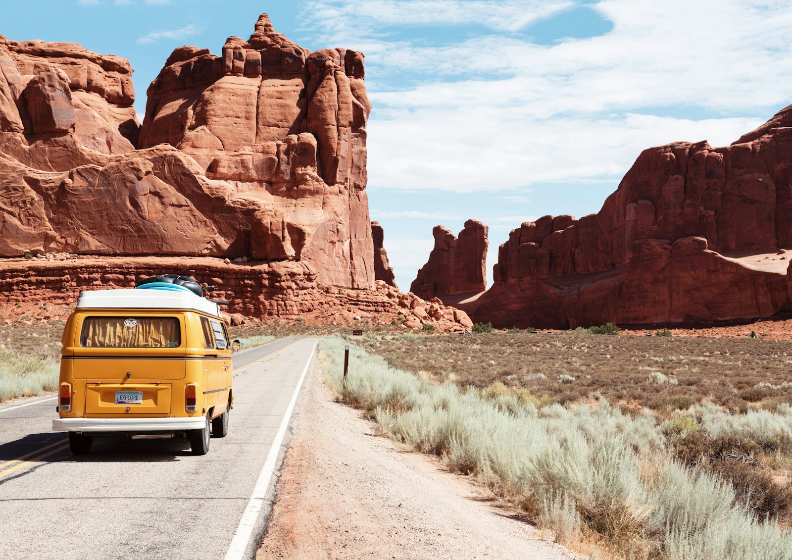 Vintage yellow camper van driving down a desert highway surrounded by towering red rock formations