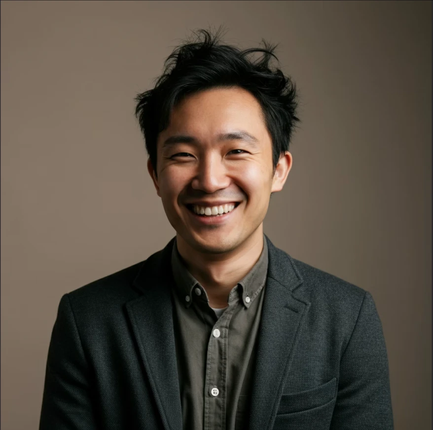 Portrait of a smiling Asian man wearing a dark collared shirt against a beige background.