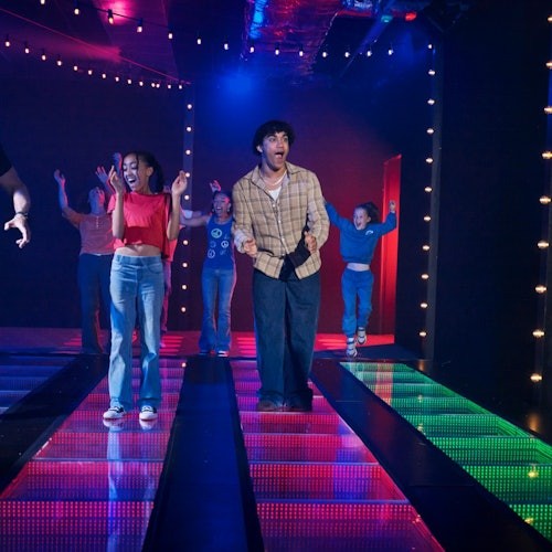 人們在五顏六色、燈光閃爍的舞池上充滿活力地跳舞,背景微弱的燈光映襯著這一切。