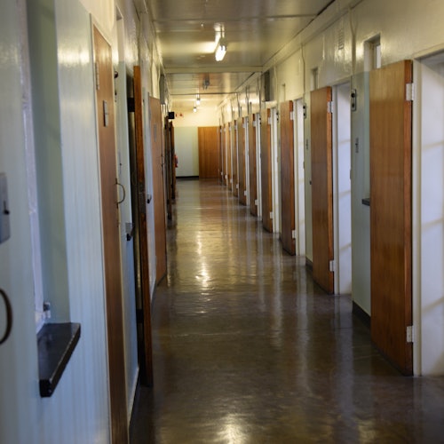 一條漫長的空走廊,幾扇木門微微打開,頭頂上有荧光燈照明。