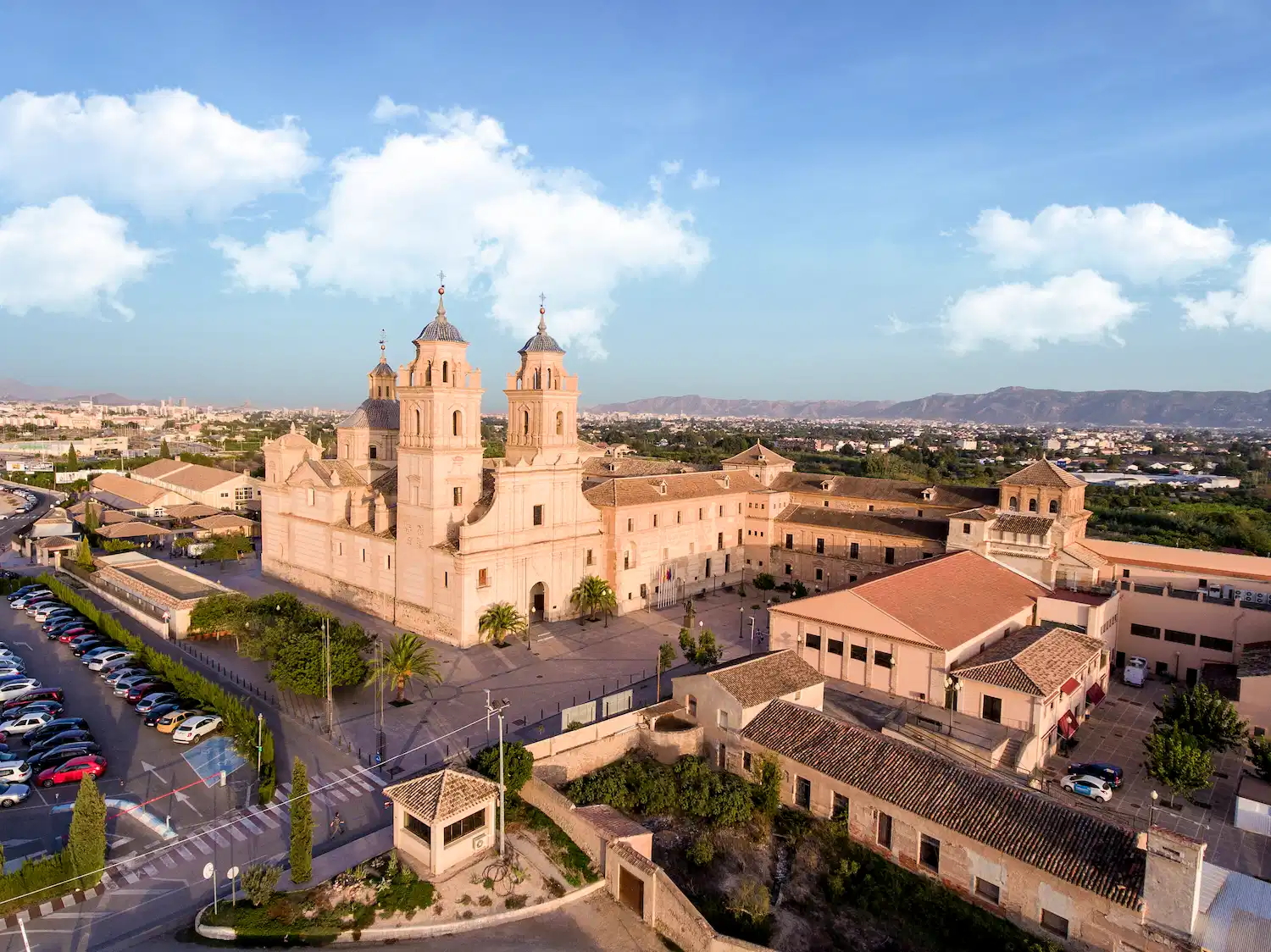 Aerial view of UCAM European University featuring historic architecture surrounded by parking and rural landscape under a bright blue sky.