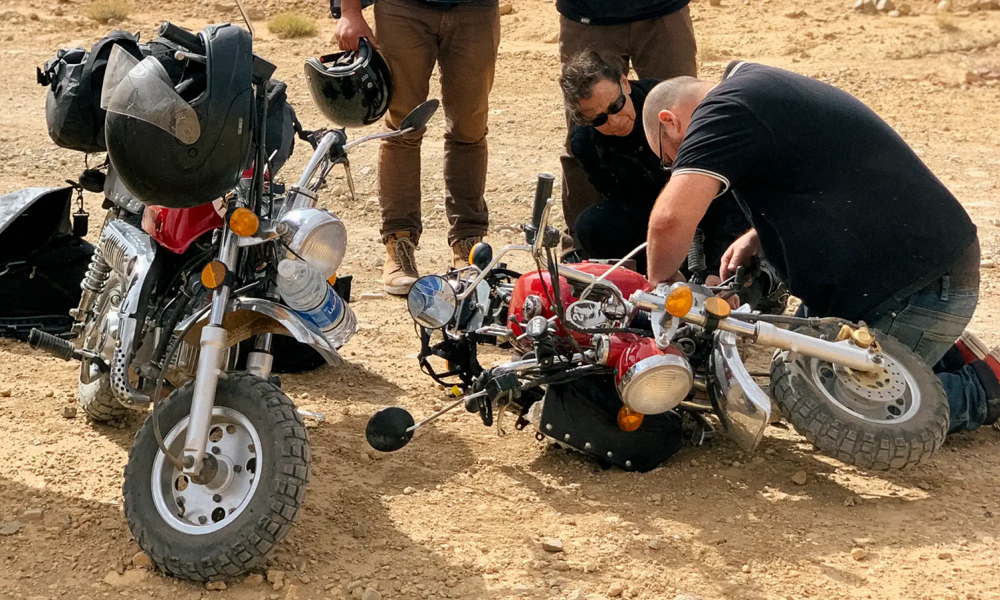 Two people working on a motorcycle while two others watch.