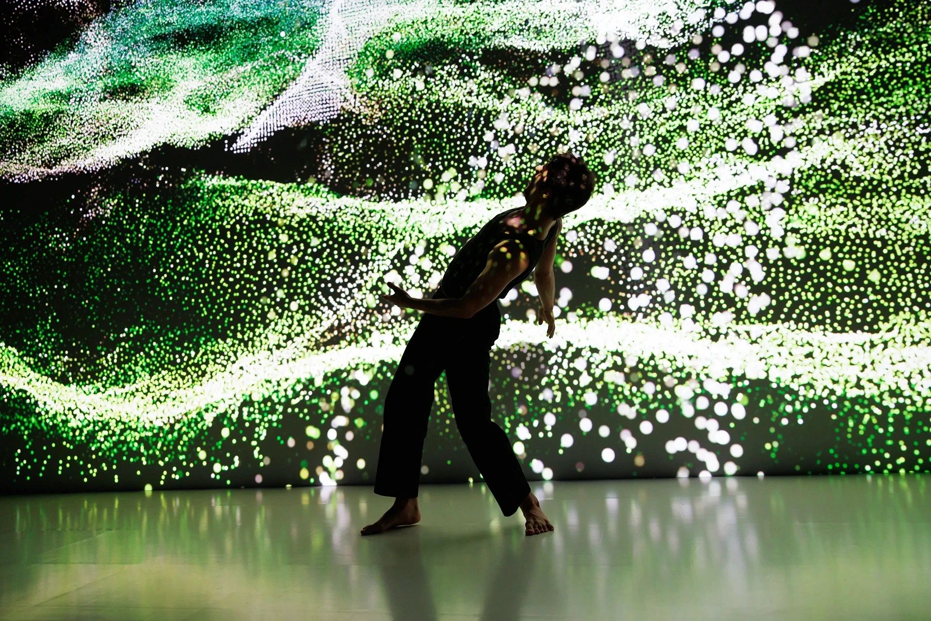 Dancer in black against green particle light display