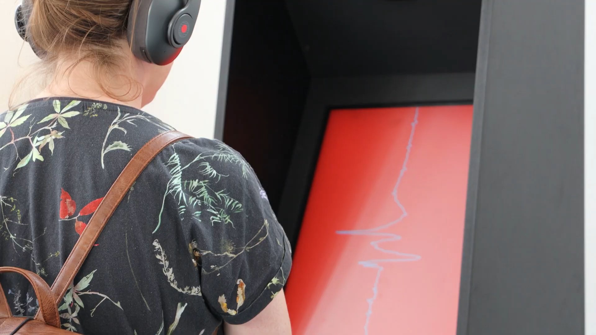 Person with headphones observes red screen with waveform.