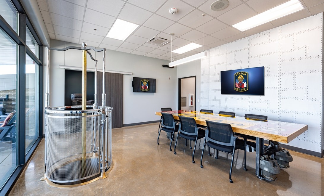 Conference room with brass fire pole and crew table at Denton Fire Station 9, by Martinez Architects
and Parkhill
