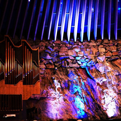 Kiviseinä, jossa on sininen ja violetti valaistus, suuren urkujen ja teräväkärkisten kattopalkkien vieressä.